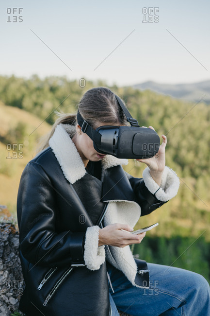 Portrait of a beautiful young woman wearing virtual reality glasses typing on a smartphone