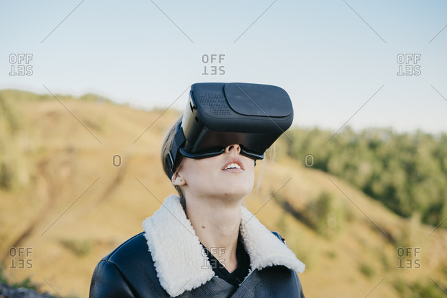 Portrait of a beautiful young woman in virtual reality glasses looking up at the sky