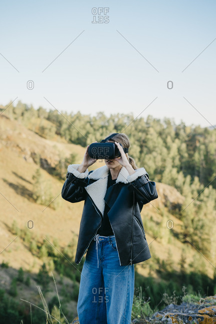 Portrait of a beautiful young woman wearing virtual reality glasses while sitting outside in a beautiful forest