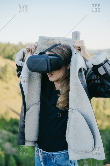 Portrait of a beautiful young woman wearing virtual reality glasses while buttoning her jacket