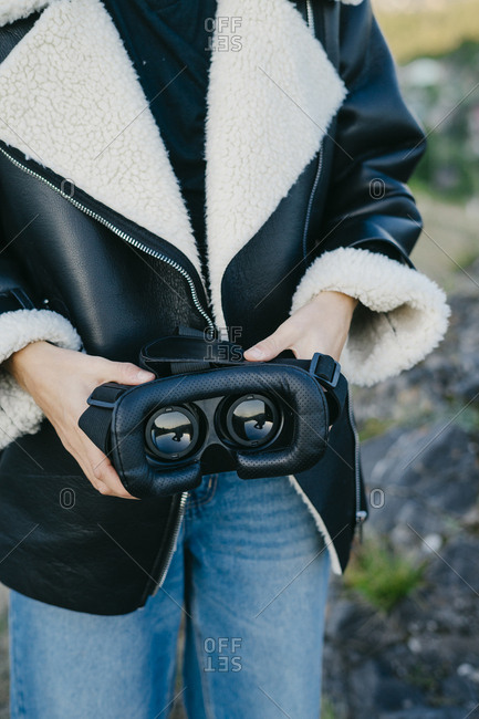 Portrait of a beautiful young woman in a black jacket holding virtual reality glasses for a smartphone