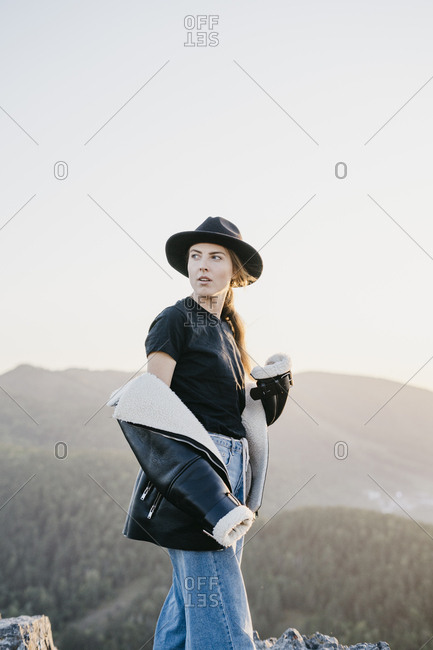 Portrait of a beautiful young woman in a black jacket and hat laughing while sitting on a rock
