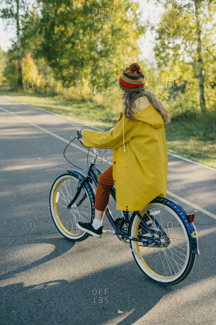 Beautiful young woman in a yellow raincoat riding a retro bike on a path in the park