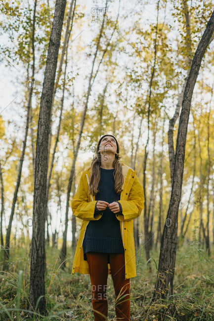 Beautiful young woman in a yellow coat standing looking out at the fall forest
