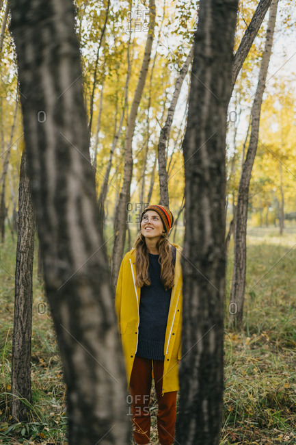 Beautiful young woman in a yellow coat standing looking out at the fall forest