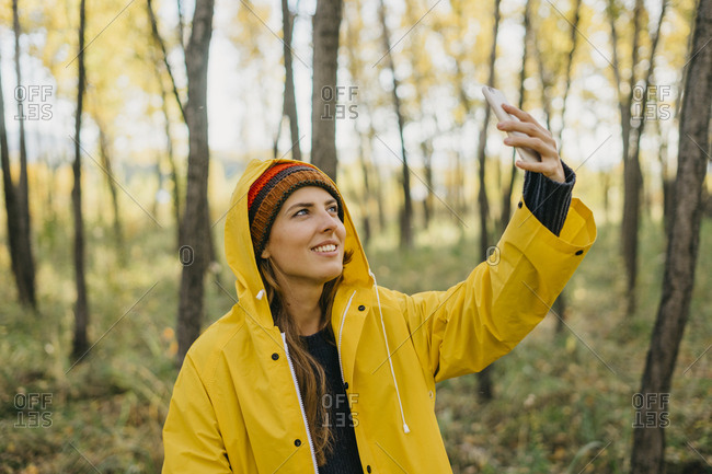 Portrait of a beautiful young woman in a yellow raincoat and knitted hat taking a selfie