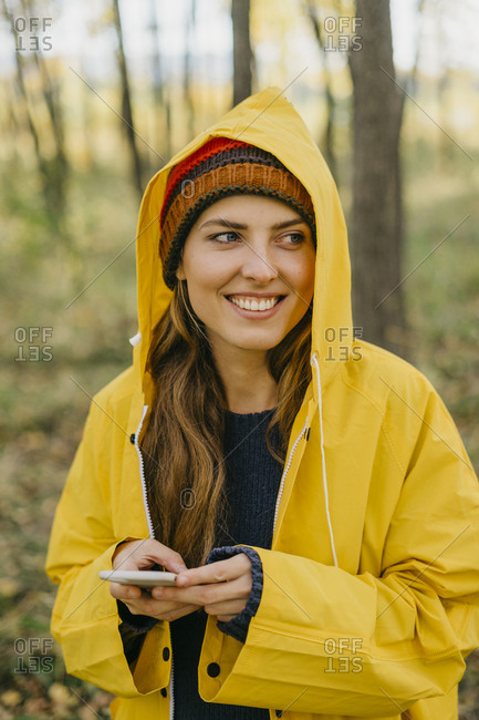 Portrait of a beautiful young woman in a yellow raincoat and knitted hat typing a message on her smart phone