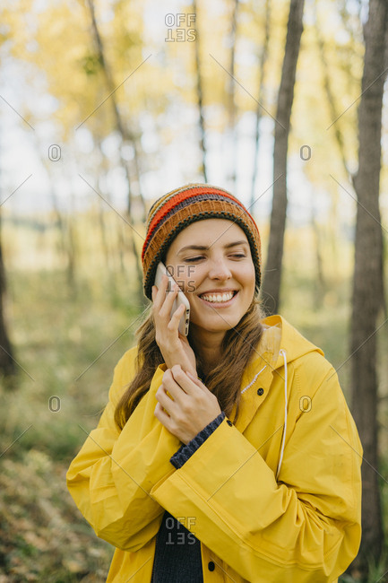 Portrait of a beautiful young woman in a yellow raincoat and knitted hat talking on her cell phone
