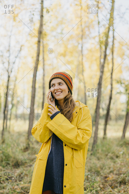 Portrait of a beautiful young woman in a yellow raincoat and knitted hat talking on her cell phone