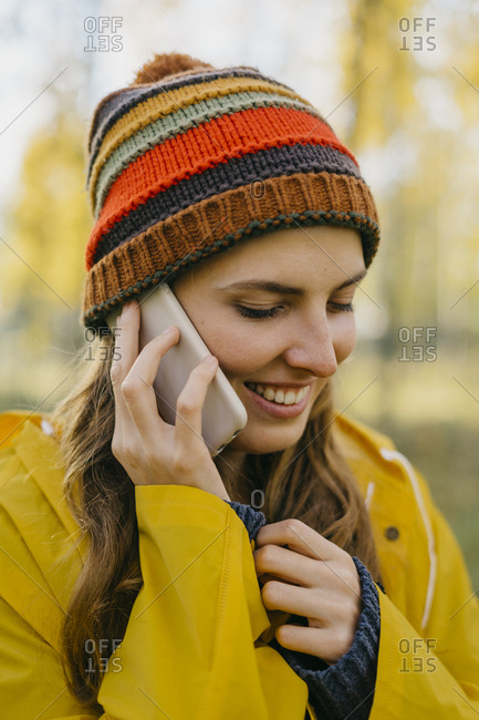Portrait of a beautiful young woman in a yellow raincoat and knitted hat talking on her cell phone