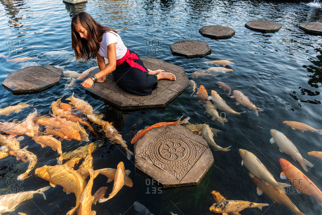 Woman feeding koi fishes in Water Palace in Bali, Indonesia