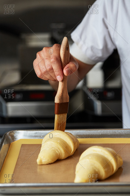 Person using pastry brush to prepare croissants