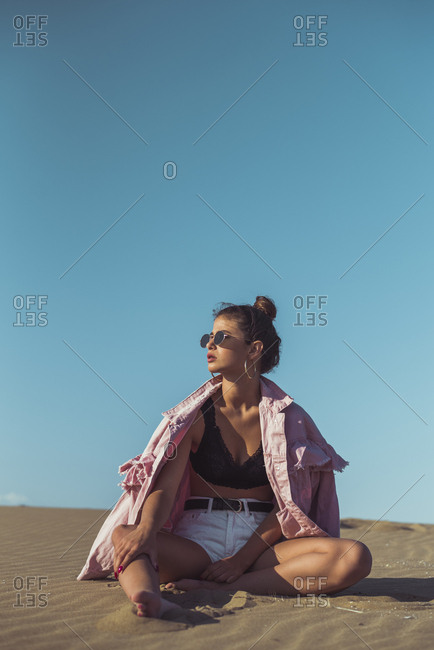 Teenage girl sitting on beach dune against blue sky