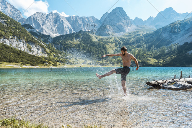 Austria, Tyrol, Young man at Lake Seebensee kicking water, having fun