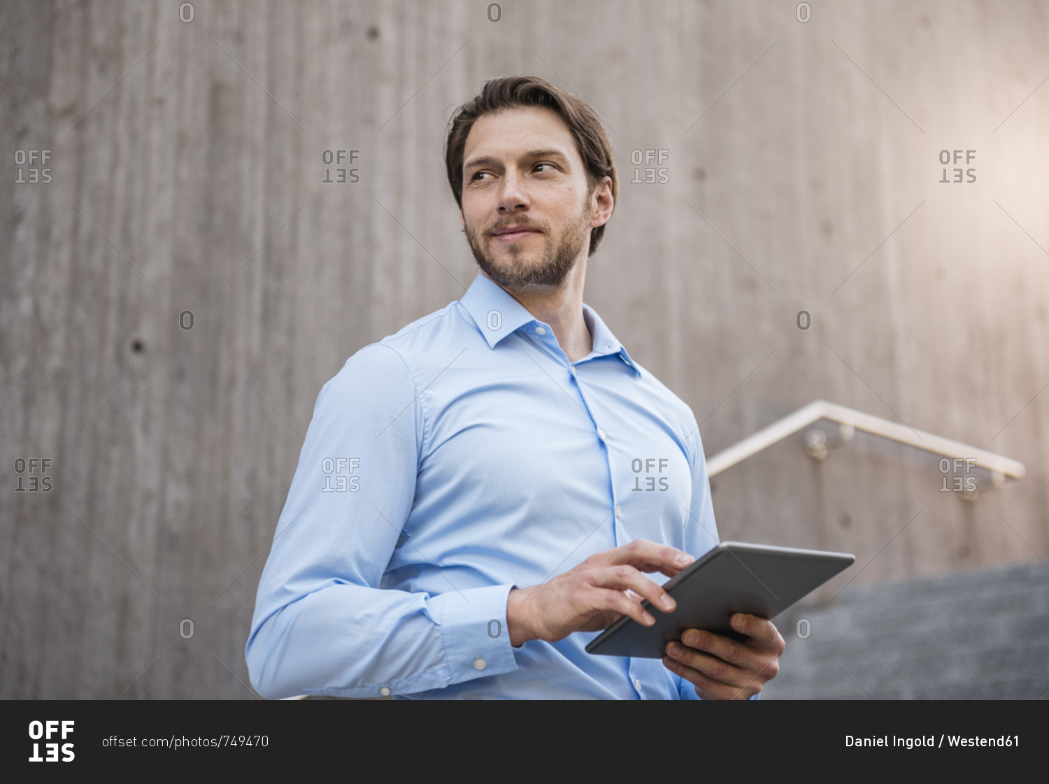 Smiling businessman on stairs with tablet looking sideways