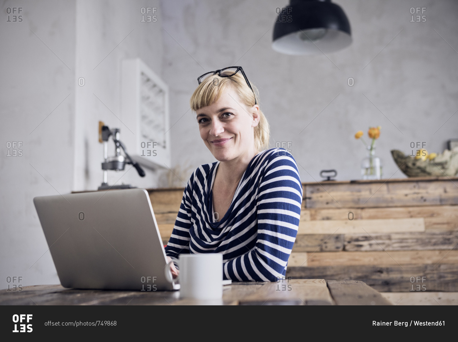 Portrait of smiling woman sitting at table with laptop and coffee mug