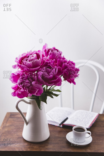 Pink peonies in a pitcher with a journal on a wooden table