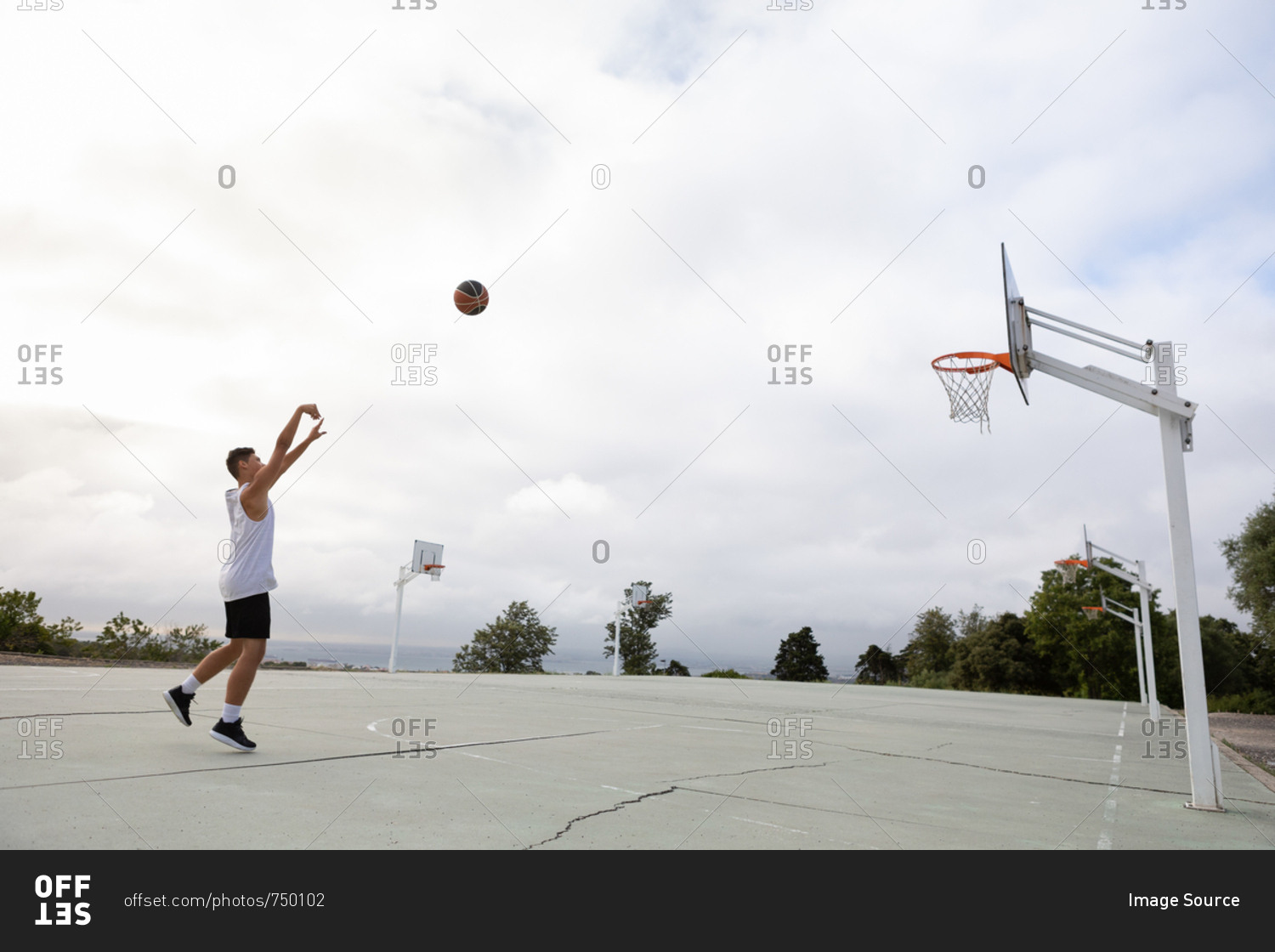 Male teenage basketball player throwing ball toward basketball hoop