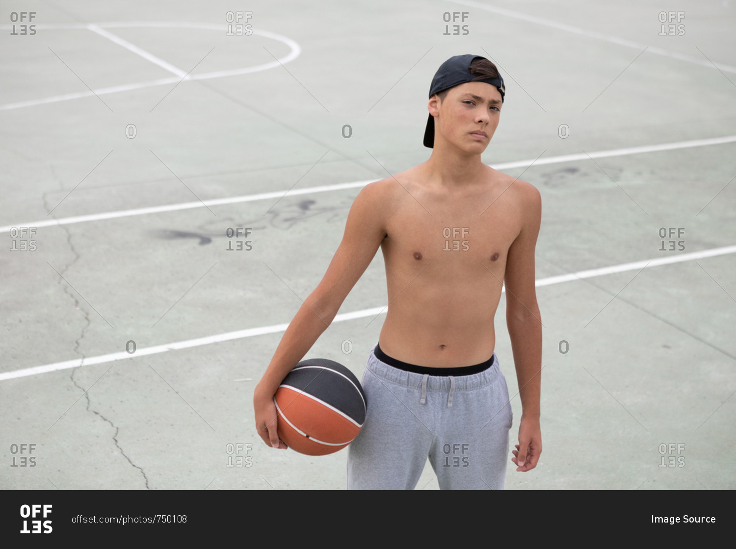 Male teenage basketball player with ball on basketball court, portrait