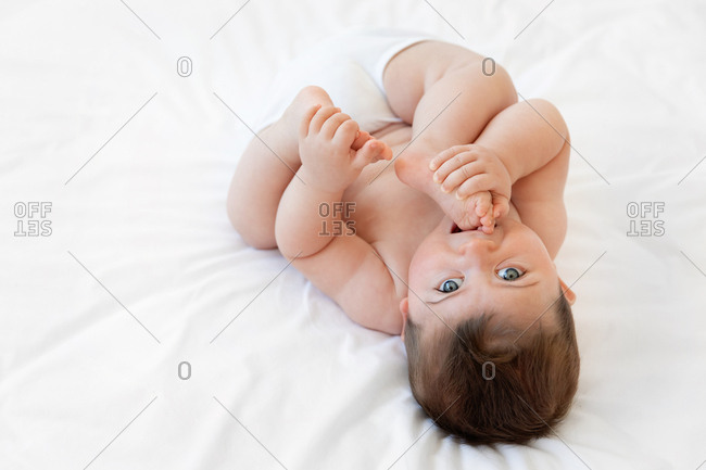 Cute chubby baby chewing on feet on a bed