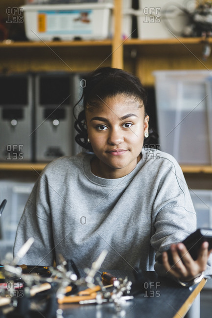 Portrait of confident female teenage student sitting with science project at desk in classroom at high school