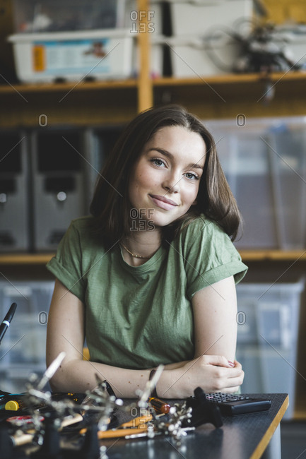 Portrait of smiling female student sitting with science project at desk in classroom at high school