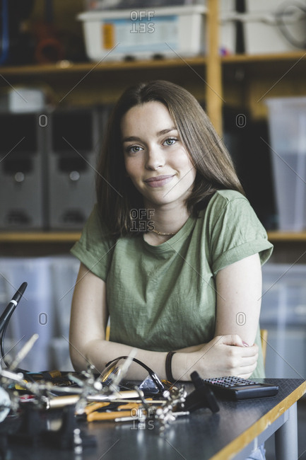 Portrait of confident female student sitting with science project at desk in classroom at high school