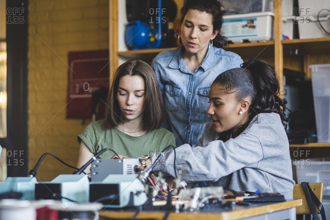 Female teacher looking at high school teenage students preparing robot on desk in classroom