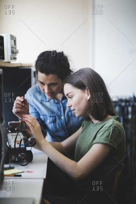 Female teacher assisting teenage student preparing robot on desk in classroom at high school