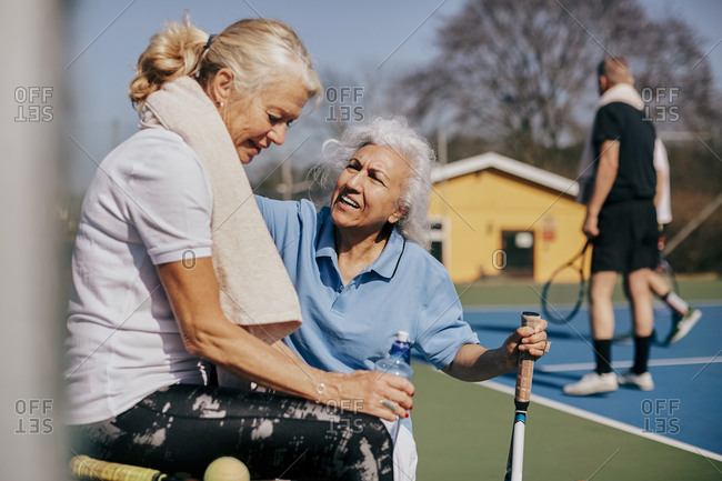 Senior woman talking to tired friend at tennis court