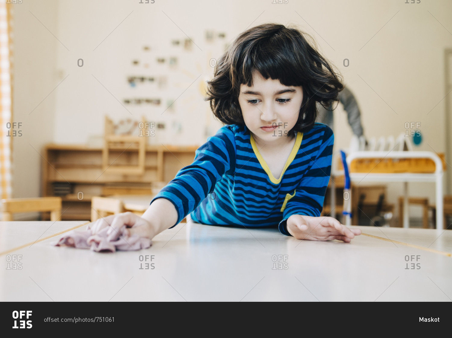 Boy cleaning table with dish cloth in child care classroom