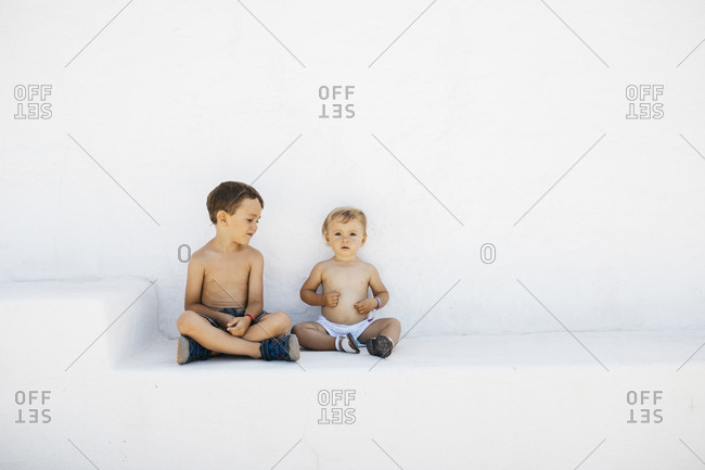 Infant boy with elder brother sitting on white steps outdoors