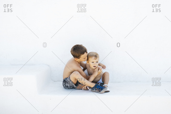 Little boy embracing adorable infant brother sitting on white steps