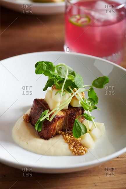 A tapas style dish of pork belly with apples, parsnip puree and pickled mustard seeds and pea shoots.  Nearby a Beet cocktail of boz mexcal, beet simple syrup, lime, and a slice of jalapeno.