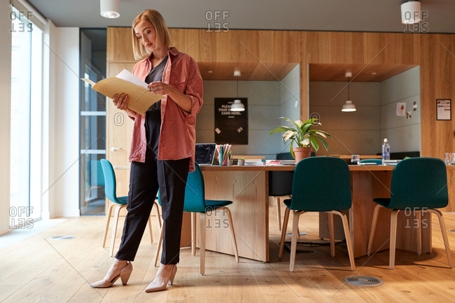 Young creative businesswoman standing in her office reading a document, full length, low angle