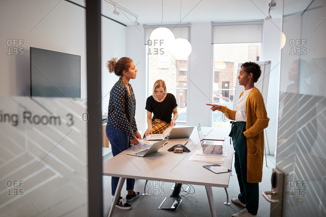 Young creative business team standing around a table at a brainstorm meeting in an office, seen from doorway