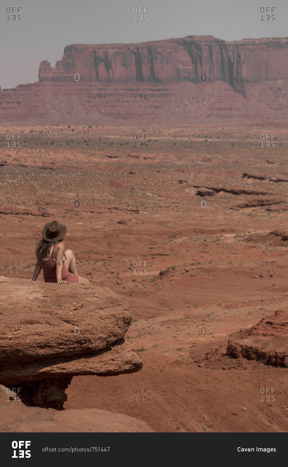 Rear view of female hiker looking at buttes while sitting on rocks against sky in Monument Valley Tribal Park during sunny day