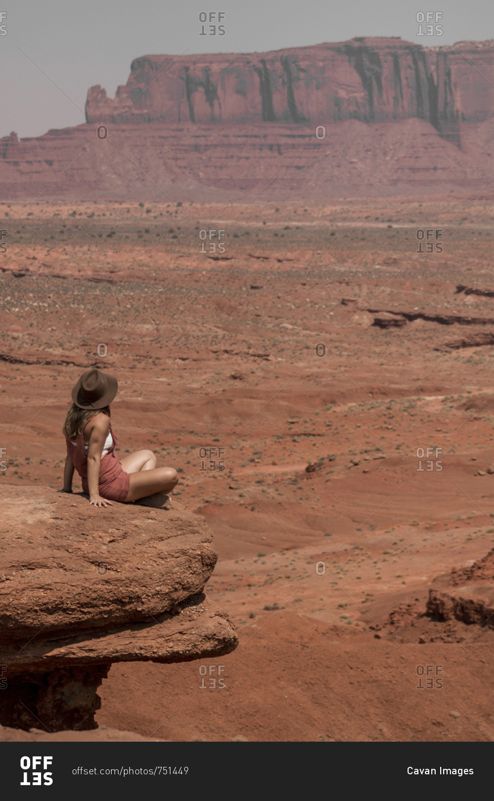 Female hiker looking at buttes while sitting on rocks against sky in Monument Valley Tribal Park during sunny day