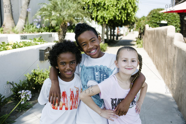 Portrait of confident smiling siblings standing on footpath in city