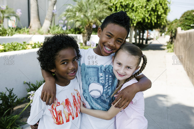 Portrait of smiling siblings standing on footpath in city