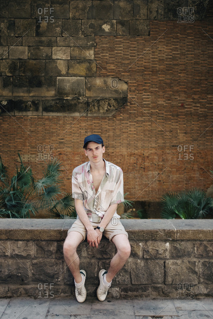 Portrait of confident man wearing cap while sitting on retaining wall