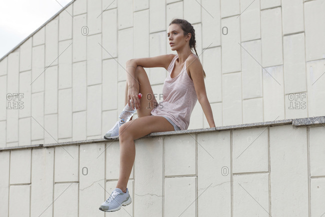Low angle view of thoughtful woman in sports clothing looking away while sitting on retaining wall