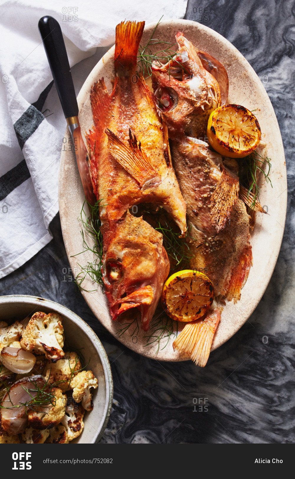 Whole cooked fish served with grilled lemon halves and roasted cauliflower
