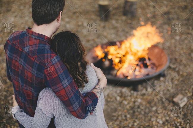Couple with their arms around each other enjoying an outdoor fire