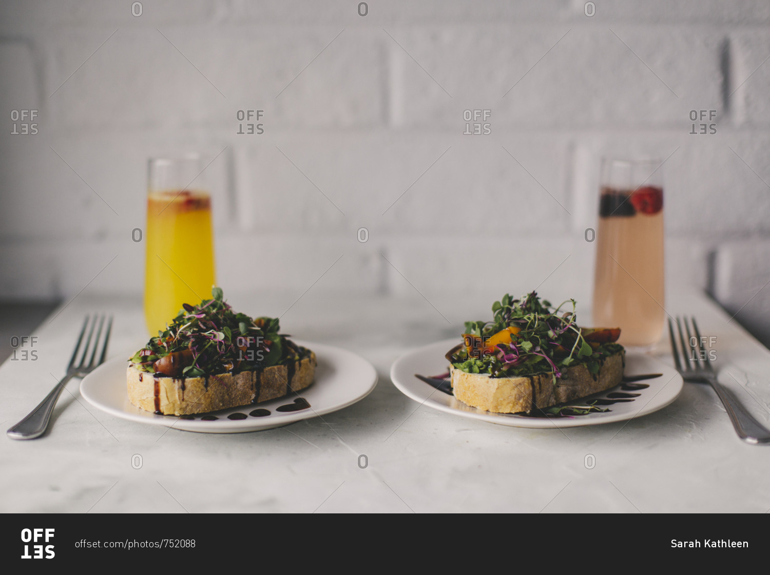 Two plates of toast topped with microgreen salad, tomatoes, and balsamic vinegar served with drinks