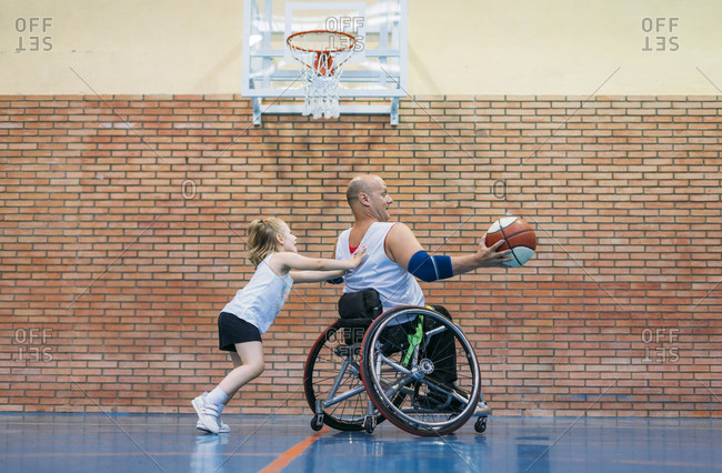 Disabled sport men and little girl in action while playing indoor basketball