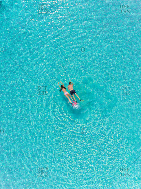 Aerial view of man and woman with masks and flippers snorkeling in turquoise water.