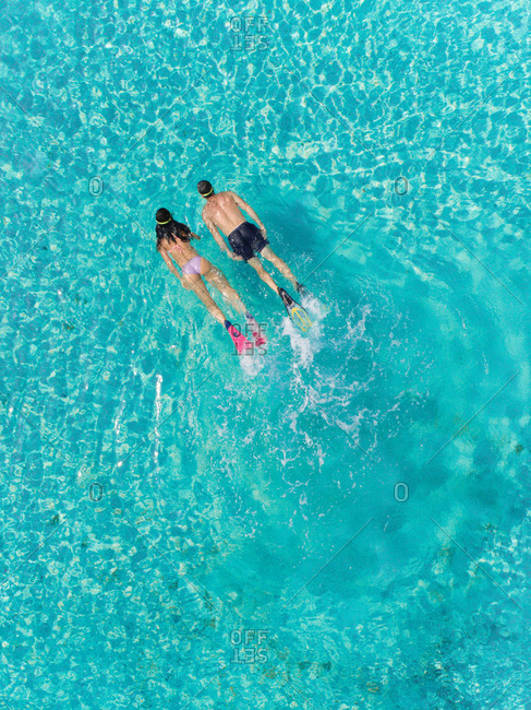 Aerial view of man and woman snorkeling next to each other in masks and flippers in turquoise sea.