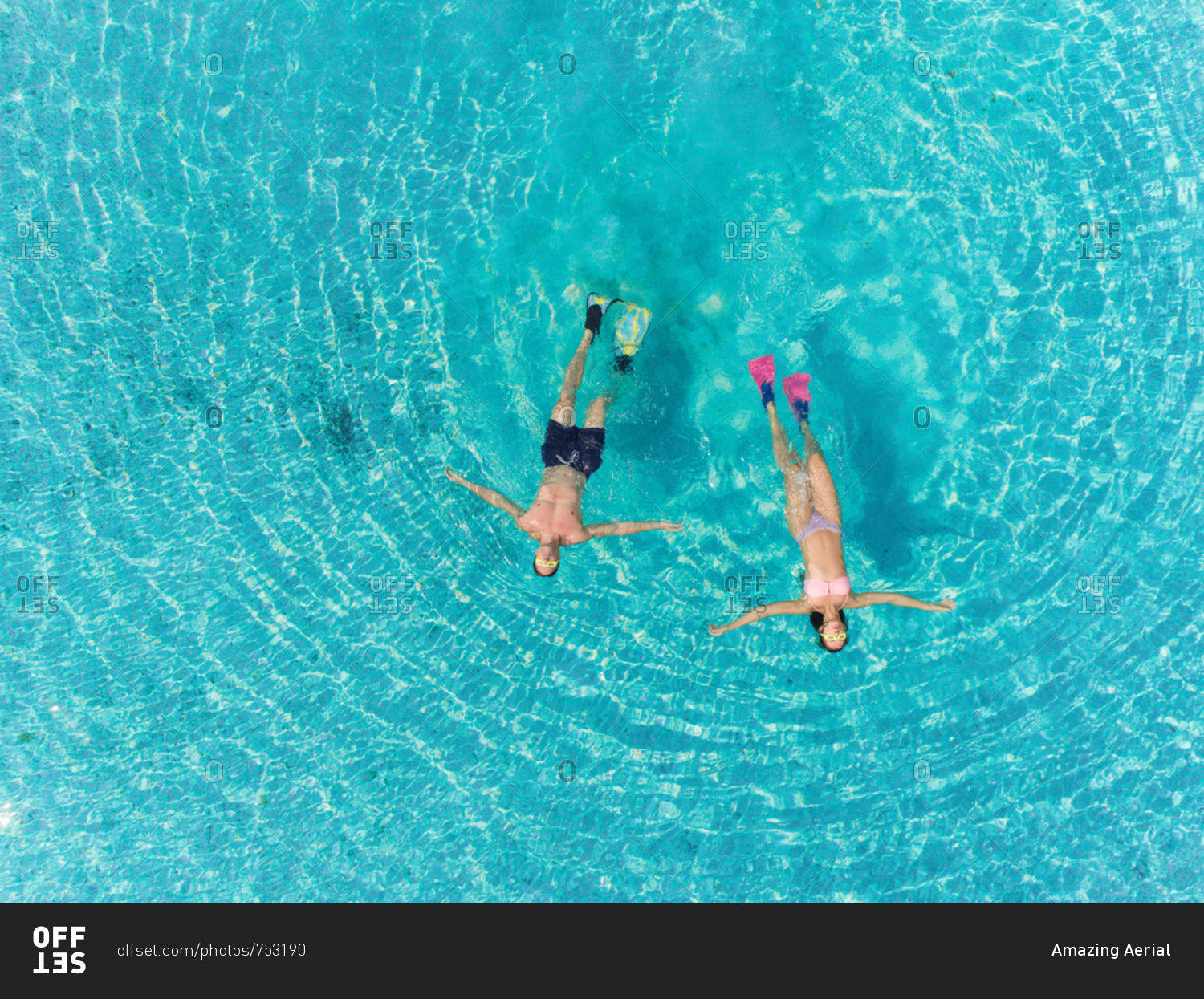 Aerial view of man and woman with masks and flippers swimming on their backs in clear sea.
