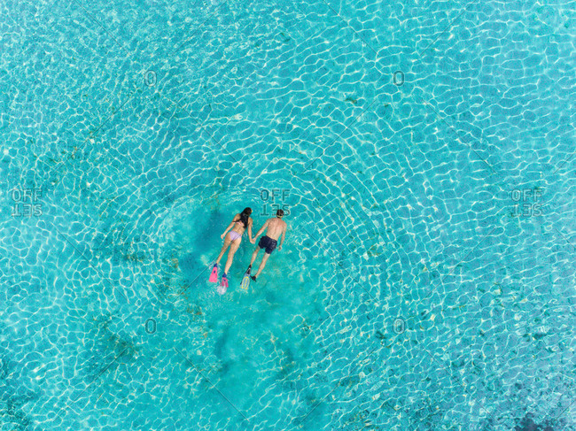 Aerial view of man and woman swimming and snorkeling with masks and flippers in clear sea.